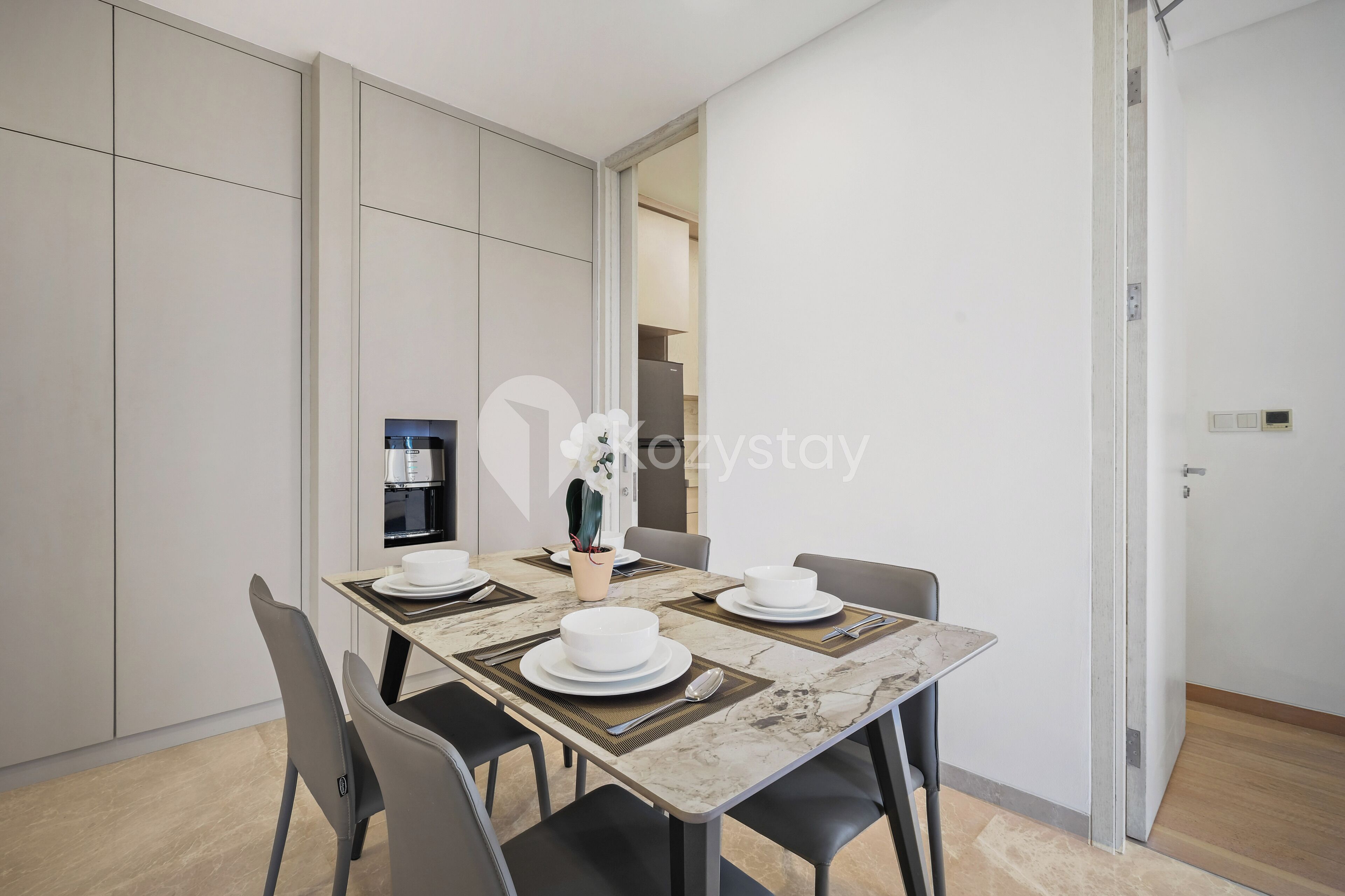 Un espace repas moderne avec une table en marbre, quatre chaises et une cuisine en arrière-plan.