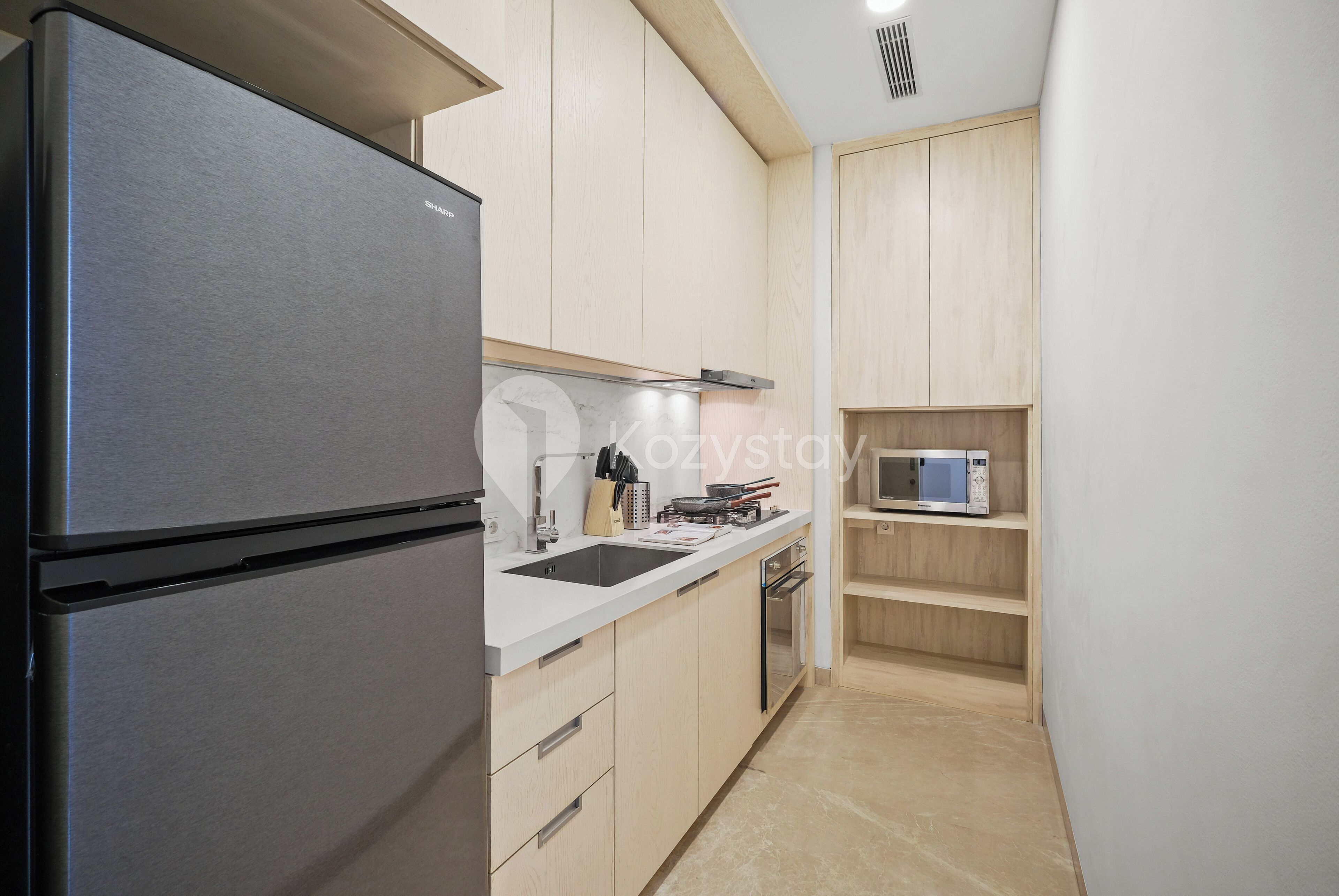 A compact kitchen with a stainless steel refrigerator, a microwave, and wooden cabinets.