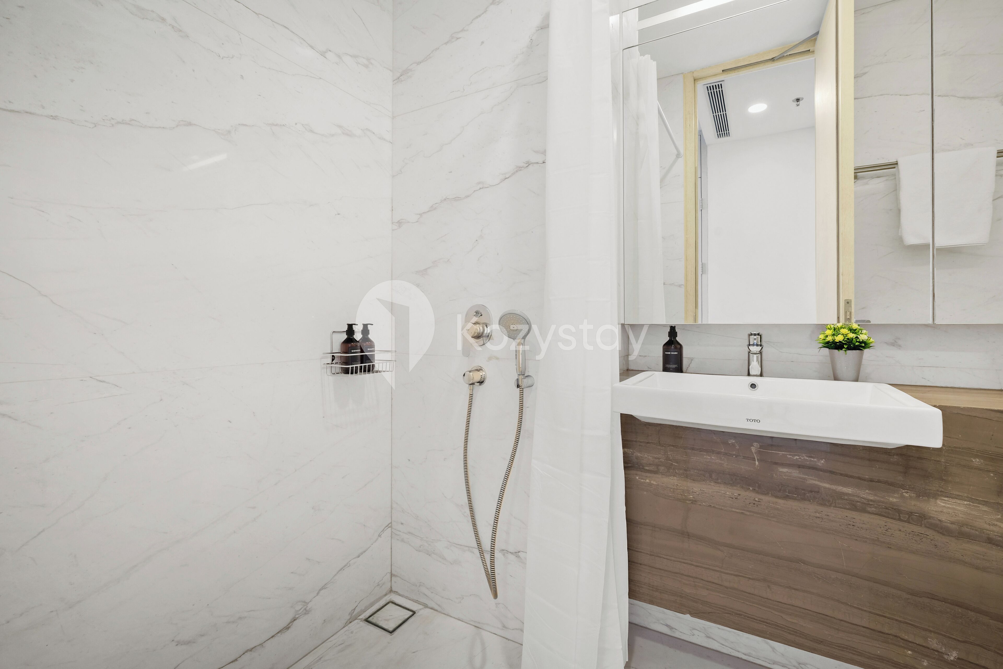 A modern bathroom with a marble wall, a wooden vanity, a white sink, and a shower with a handheld showerhead.