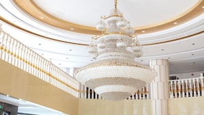 Un gran candelabro en un vestíbulo amplio con techo alto y una decoración en blanco y dorado.