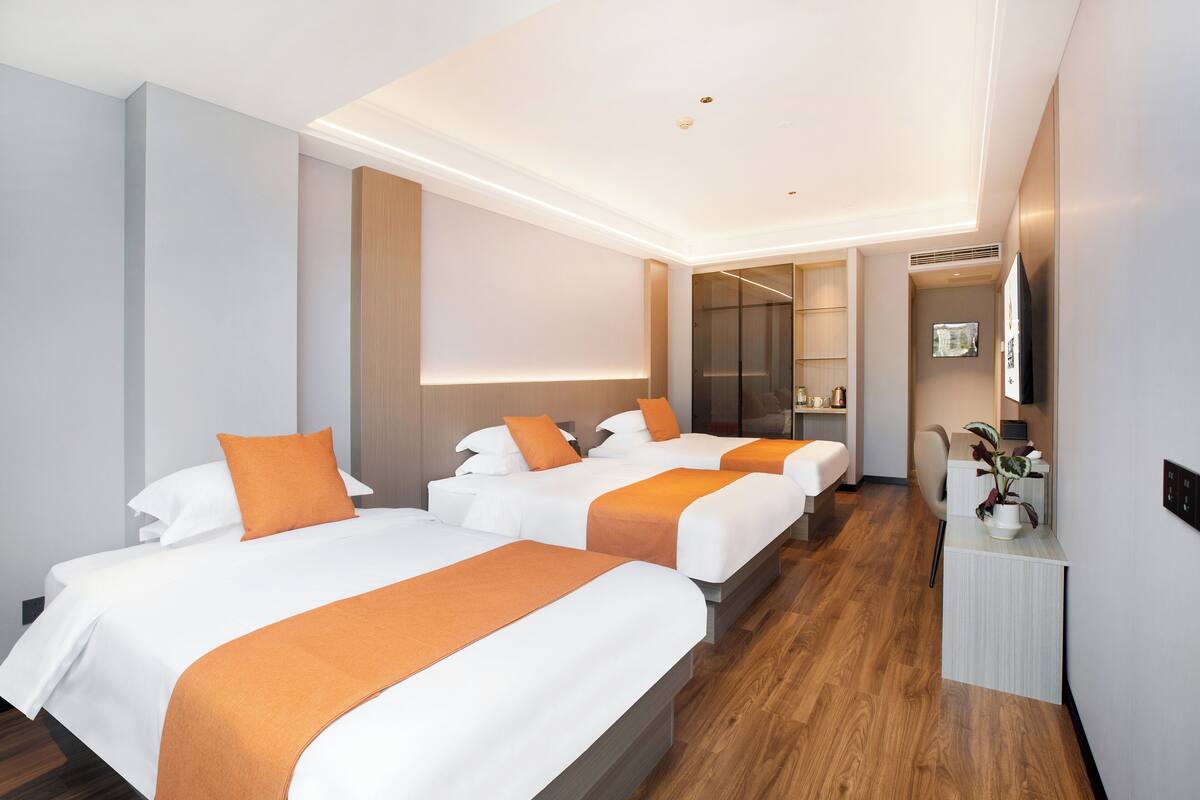 Habitación de hotel con tres camas, un escritorio y un espejo.