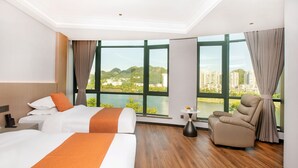 Habitación de hotel con dos camas, un sofá, vista a un lago y al paisaje urbano, y suelo de madera.