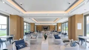 A spacious, modern lounge area with comfortable seating, a central coffee table, and large windows offering views of the outdoors. - Vogue | Downtown with Direct Access to Dubai Mall (Dubai)