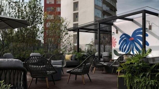 Un espacio al aire libre con sillas de mimbre, un sofá acolchado y una pared decorativa con diseño floral.
