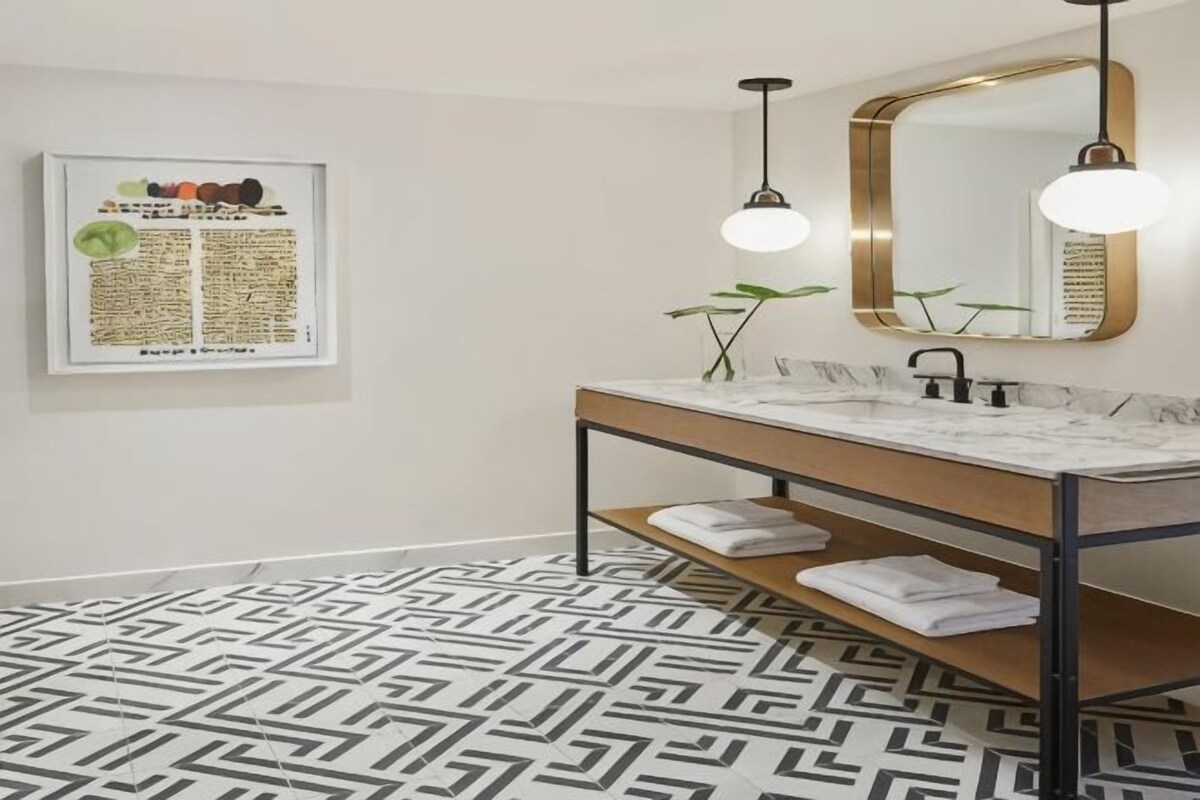 A modern bathroom with a marble sink, a wooden vanity, a large mirror, and a geometric patterned floor.