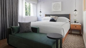 Un dormitorio moderno con un sofá verde, una mesa redonda, una cama con ropa de cama blanca y una mesita de noche con lámpara.