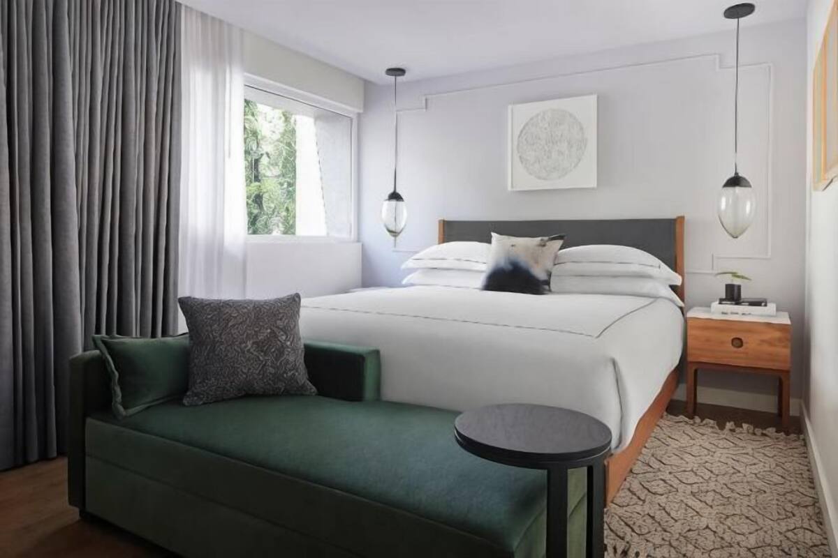 A modern bedroom with a green sofa, a round table, a bed with white bedding, and a nightstand with a lamp.