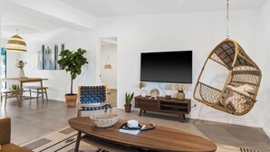 A modern living room with a wooden coffee table, a hanging chair, a flat-screen TV, and a dining area with a table and chairs. - 3-bedroom family and pet friendly just 12 minutes from Joshua Tree National Park (Joshua Tree)