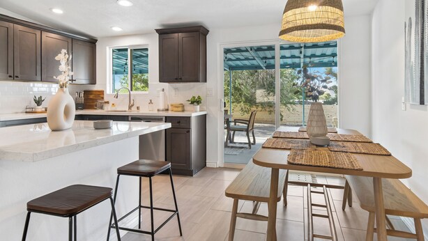 A modern kitchen with dark cabinets, a large island, and a dining area with a wooden table and stools. - 3-bedroom family and pet friendly just 12 minutes from Joshua Tree National Park (Joshua Tree)