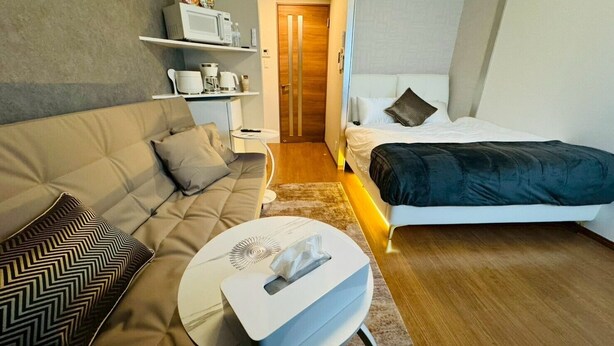 Una habitación de hotel compacta con sofá, cama, mesita de noche y microondas en un estante.