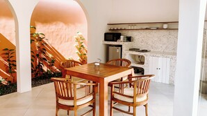 A dining area with a wooden table and chairs, a kitchen with white cabinets, and a staircase with plants. - Lovely 2BR Villa Close to The Beach (Seminyak)