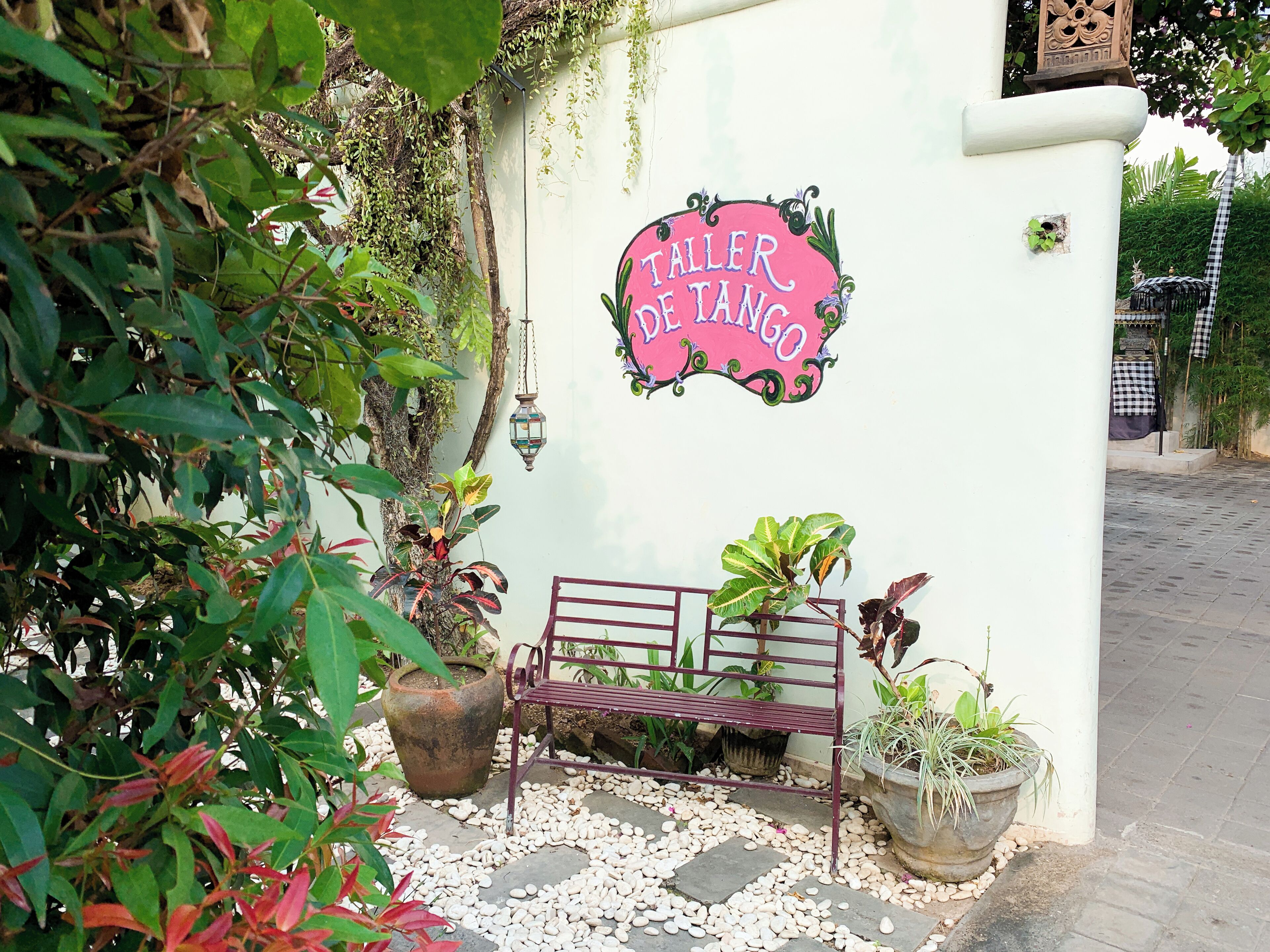 A wall with a sign reading "Taller de Tango" and a bench with potted plants.