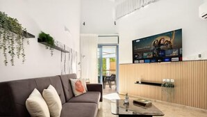 Una sala de estar moderna con un sofá marrón, una mesa de centro y un televisor en la pared mostrando un cartel de película.