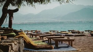 Una playa con mesas y bancos de madera, algunos con cojines.
