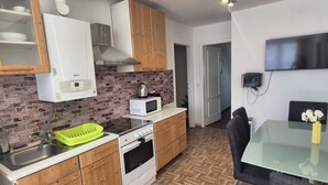 A compact kitchen with a microwave, stove, and sink, a dining area with a glass table, and a TV mounted on the wall. - 2BR Apt Next to Vienna Vibrant Center (Vienna)
