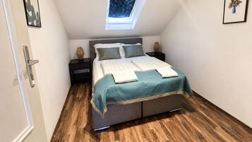 Un dormitorio con tragaluces, una cama con colcha color turquesa, dos mesitas de noche y suelo de madera.