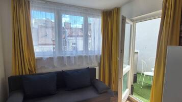 Una habitación con sofá, una puerta corrediza de vidrio que da a un balcón y un refrigerador.
