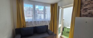 A room with a sofa, a sliding glass door leading to a balcony, and a refrigerator. - 2BR Apt Next to Vienna Vibrant Center (Vienna)