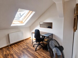 A room with a sloped ceiling, a skylight, a radiator, a desk with a chair, a mirror, and a fan. - 2BR Apt Next to Vienna Vibrant Center (Vienna)