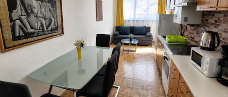 Une cuisine moderne avec un coin repas, comprenant une table en verre, des chaises noires, un canapé et un tableau accroché au mur.