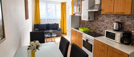 A compact kitchen with a dining area, a sofa, and a view through a window.