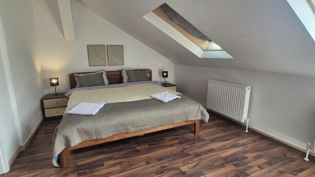 A bedroom with a sloped ceiling, a bed with a wooden frame, a radiator, and a skylight. - 2BR Apt Next to Vienna Vibrant Center (Vienna)
