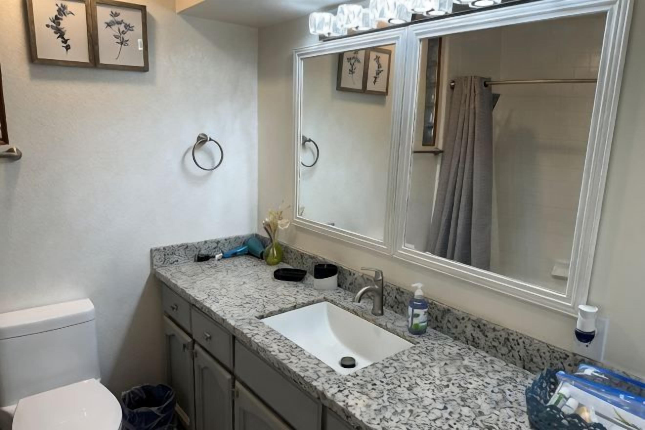 A bathroom with a granite countertop, a sink, a mirror, and a toilet.