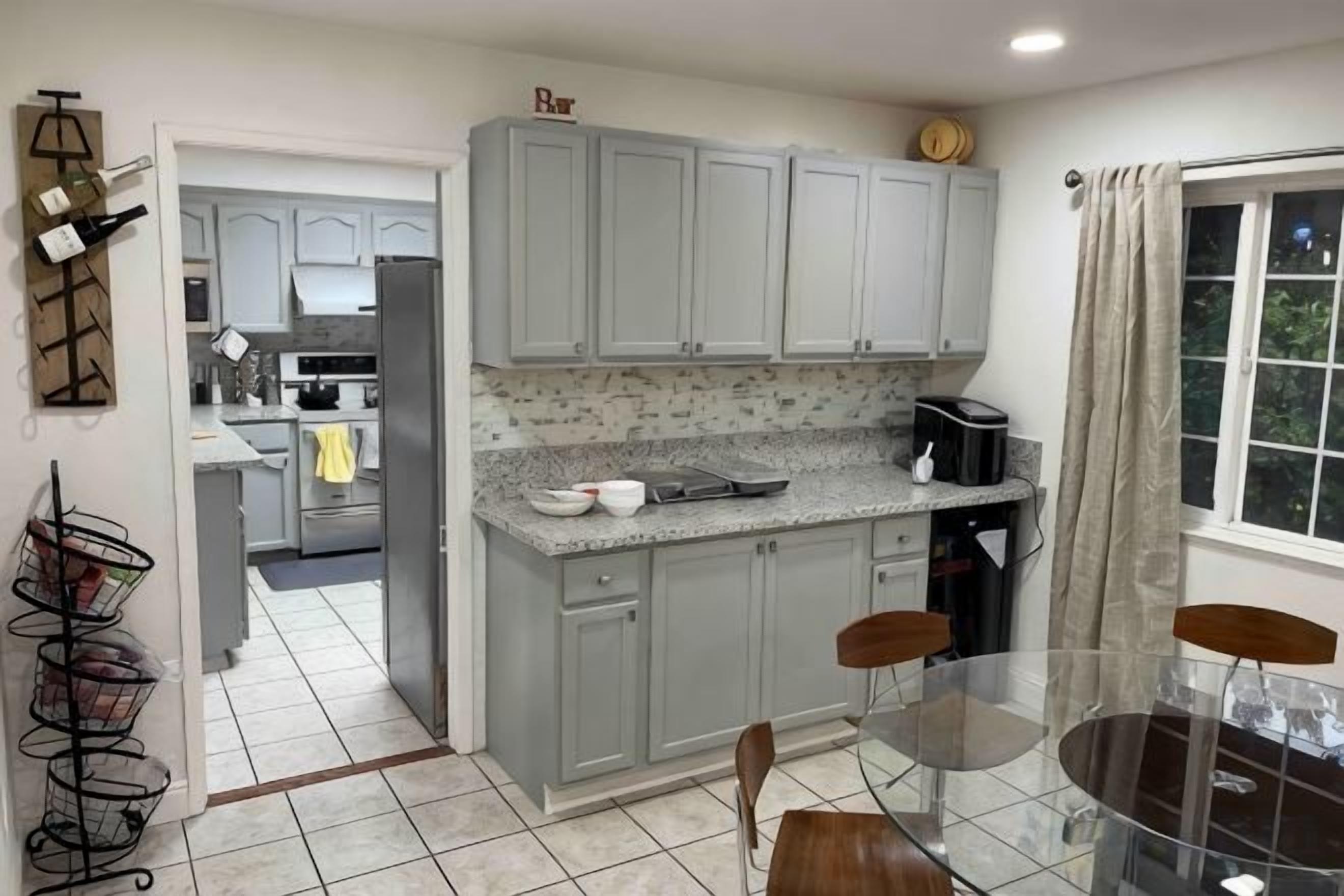 A kitchen with grey cabinets, a countertop with a coffee maker, and a dining area with a glass table and chairs.