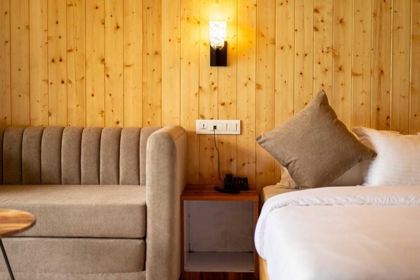 Une pièce chaleureuse avec un mur en bois, un canapé, une table de chevet avec une lampe et un lit avec des oreillers.
