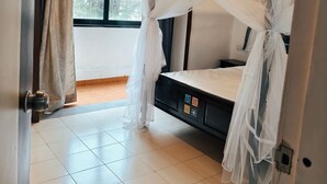 Quarto com cama sob um dossel, um ventilador de teto, janela com cortinas e piso ladrilhado.