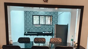 Uma área de refeições com três cadeiras, uma mesa e uma cozinha visível através de uma divisória de vidro.
