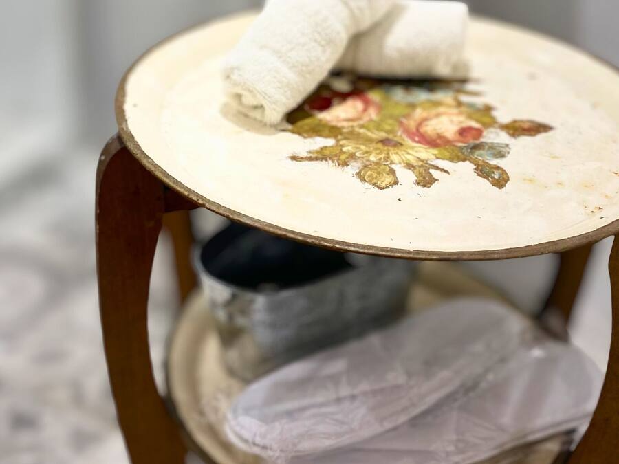 Una mesa redonda pequeña con un diseño floral en la superficie, un mantel blanco y un objeto negro debajo.