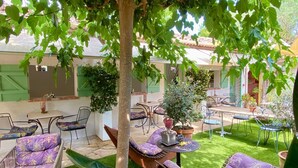 An outdoor patio area with seating arrangements, including chairs and a sofa, surrounded by lush greenery and potted plants. - Hôtel La Jabotte (Antibes)