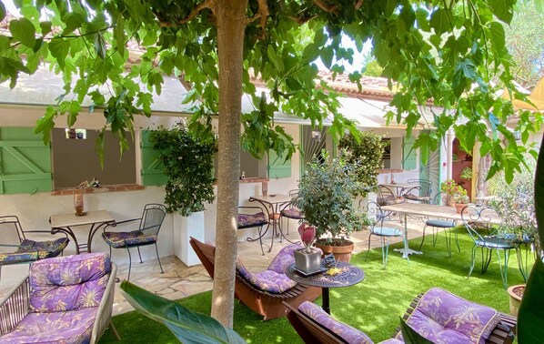 An outdoor patio area with seating arrangements, including chairs and a sofa, surrounded by lush greenery and potted plants.