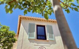 Ein Gebäude mit Fenster, Rollläden und einer Tür, im Vordergrund ein Baum.