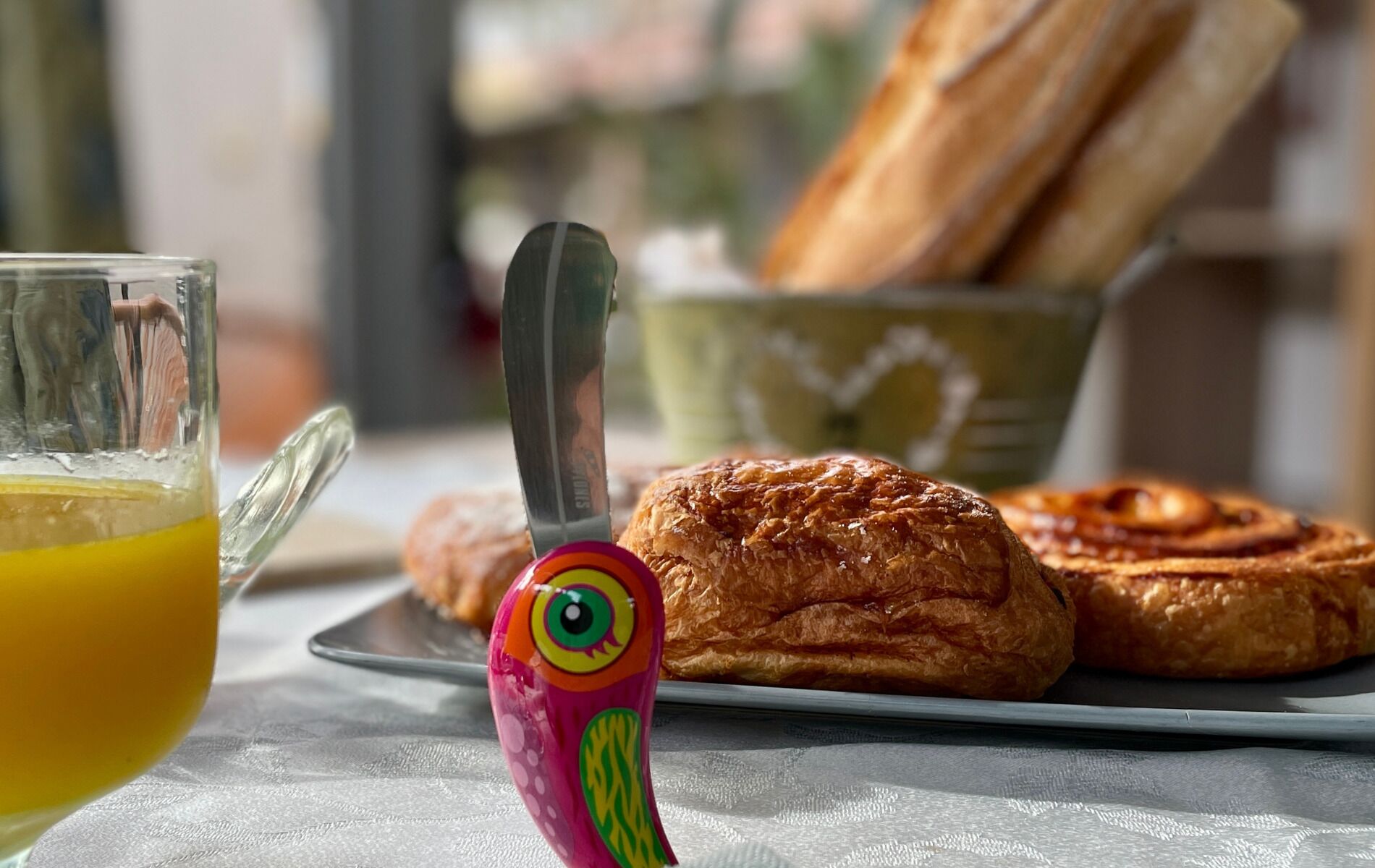 A breakfast setting with pastries, a glass of orange juice, and a colorful spoon.