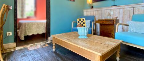 A wooden coffee table with a checkered board and a small object on it, placed in a room with a blue sofa, a wooden cabinet, and a tiled floor.