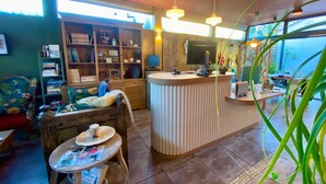 A cozy interior with a reception desk, a bookshelf, and a comfortable seating area. - Hôtel La Jabotte (Antibes)