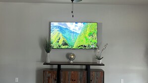 Un salon doté d’un ventilateur de plafond, d’un téléviseur à écran plat fixé sur un meuble en bois, d’un canapé en cuir et d’un tapis à motifs.
