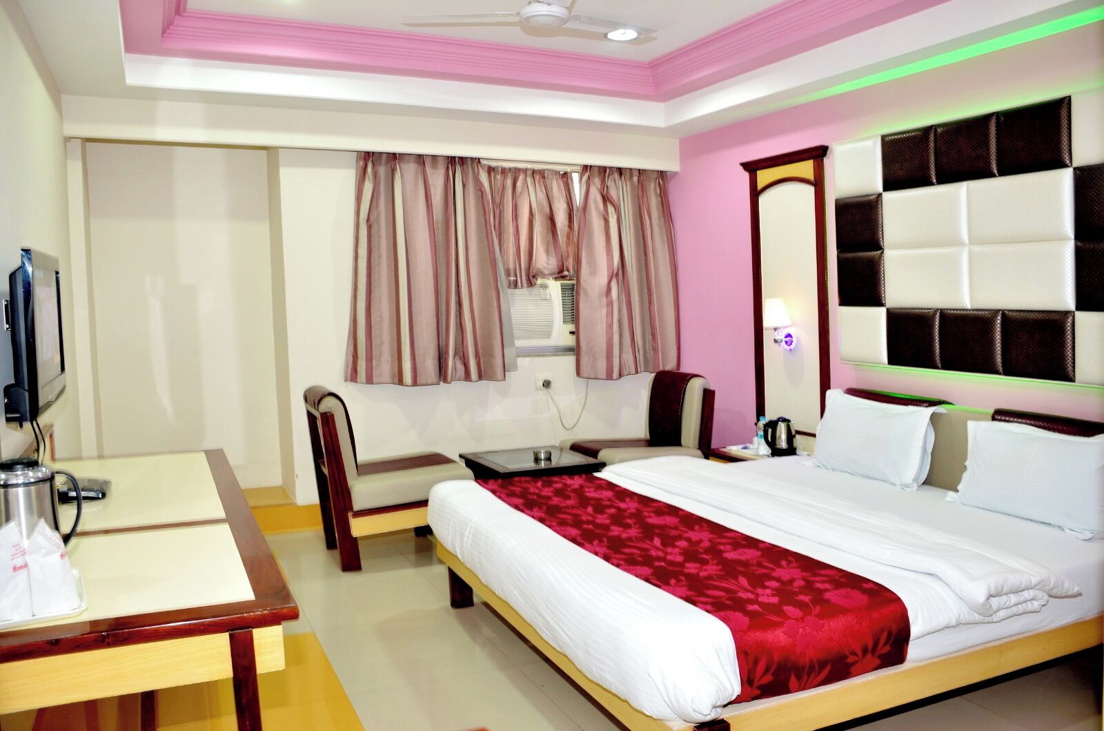 A hotel room with a bed, a desk, a chair, a television, and a window with curtains.