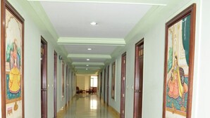 A long, well-lit corridor with framed artwork on the walls and a tiled floor. - Hotel Heeralal Bikaner (Bikaner)
