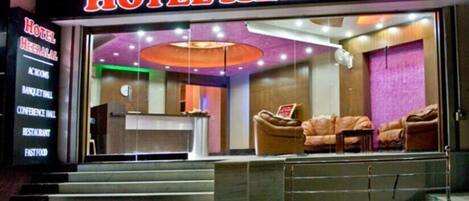Entrada de hotel con mostrador de recepción, zona de estar con sofás y una escalera que sube.