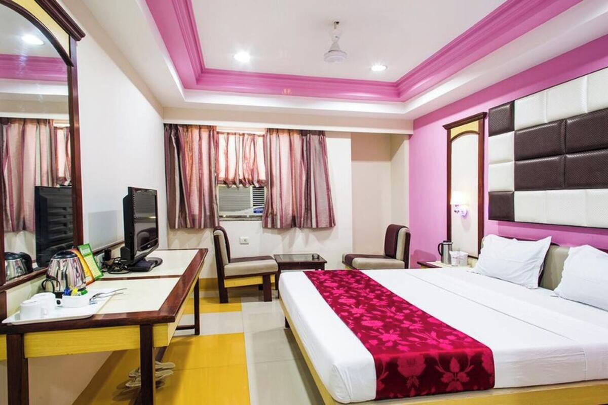 A hotel room with a bed, a desk, a chair, a television, and a window with curtains.