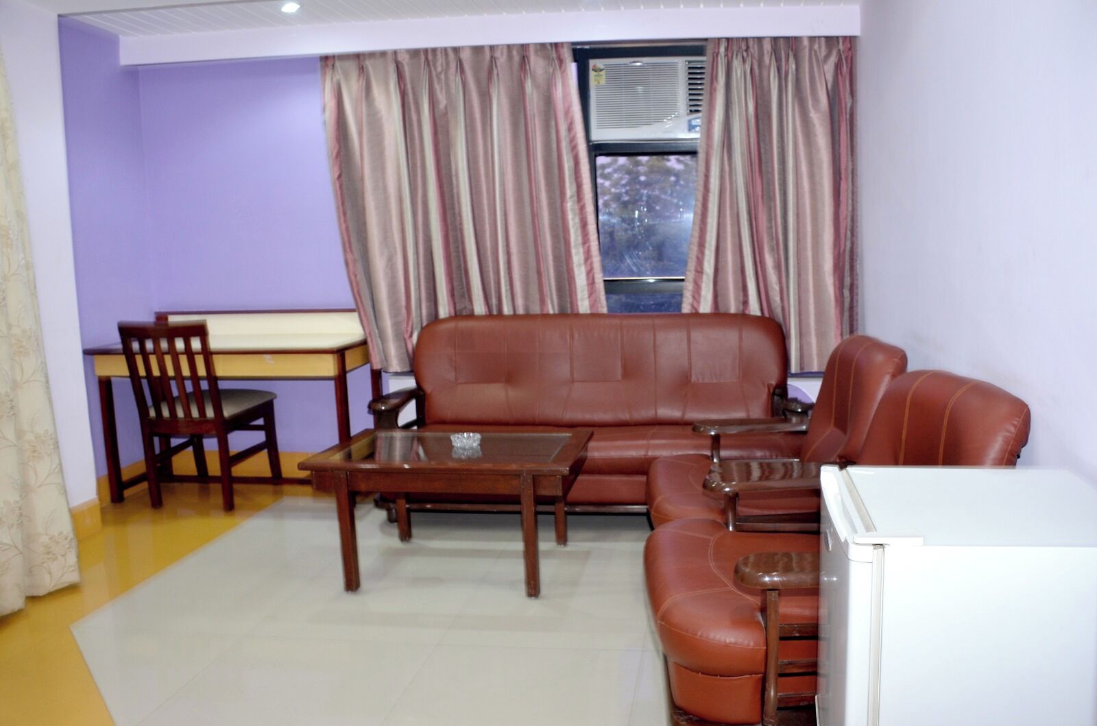 A living room with a sofa, a coffee table, a dining table with chairs, and a refrigerator.