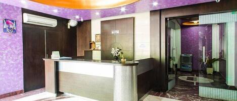 Un área de recepción con piso de mármol, un mostrador y una pared morada.