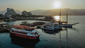 Un puerto con barcos, un edificio grande y montañas al fondo.