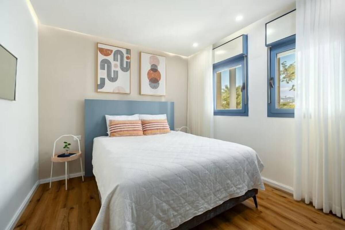 A bedroom with a bed, a chair, and two windows with curtains.