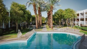 Una piscina rodeada de palmeras y vegetación, con un edificio moderno al fondo.