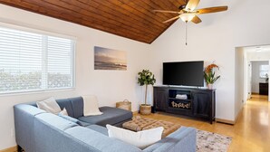 A modern living room with a sectional sofa, a flat-screen TV, a ceiling fan, and a large window with blinds. - Beach Home with Open Living & Walkability to Abbot Kinney | Venice Drift (Los Angeles)