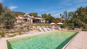 Una piscina con lettini e ombrelloni, circondata da un muro in pietra e vegetazione.